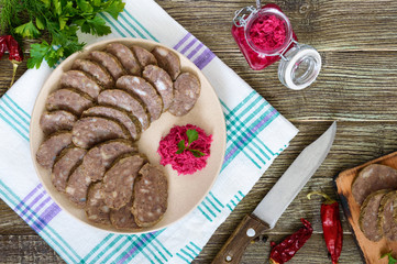 Home made dietary sausage from the liver on a wooden table. Sausage cut into pieces on a plate with horseradish sauce. Top view.
