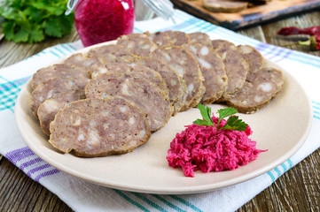Home made dietary sausage from the liver on a wooden table. Sausage cut into pieces on a plate with horseradish sauce.