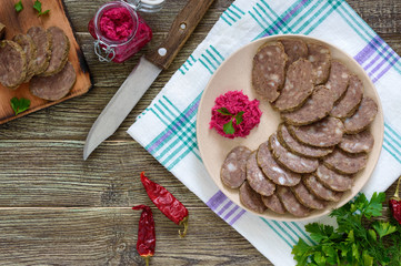 Home made dietary sausage from the liver on a wooden table. Sausage cut into pieces on a plate with horseradish sauce. Top view.