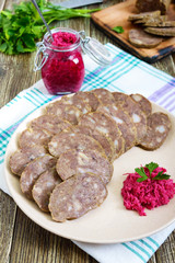 Home made dietary sausage from the liver on a wooden table. Sausage cut into pieces on a plate with horseradish sauce.