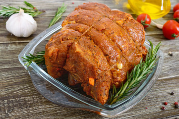 A large piece of pork meat on a wooden table, marinated in spices, stuffed with garlic and carrots, ready for baking. Preparation of a festive meat dish.