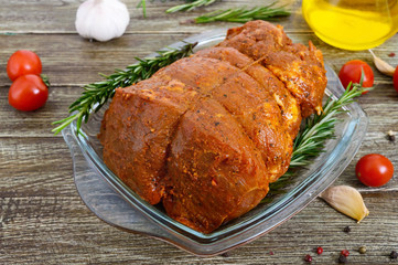 A large piece of pork meat on a wooden table, marinated in spices, stuffed with garlic and carrots, ready for baking. Preparation of a festive meat dish.
