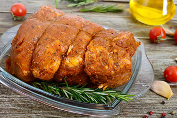 A large piece of pork meat on a wooden table, marinated in spices, stuffed with garlic and carrots, ready for baking. Preparation of a festive meat dish.