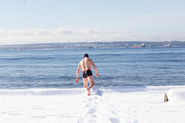 Man swimming in the cold ocean in winter. Taken in Ambleside Park, West Vancouver, British Columbia, Canada.