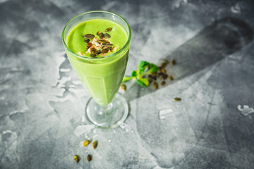 Healthy green smoothie with spinach, banana and pumpkin seeds on dark.