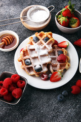 Traditional belgian waffles with fresh fruit and powder sugar on wooden board
