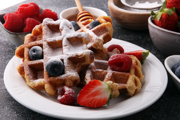 Traditional belgian waffles with fresh fruit and powder sugar on wooden board