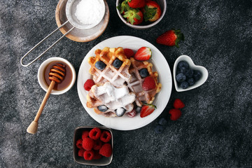 Traditional belgian waffles with fresh fruit and powder sugar on wooden board