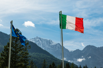 Italian Alps. Italian flag with Monte Rosa background (4.636 m), one of the highest mountains in Europe.Tourism concept on the Italian mountains. Macugnaga village. Focus on the Italian flag