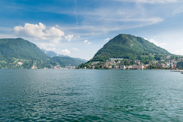 Lugano, Canton Ticino, Switzerland. Lugano lakefront and Lugano lake with the San Salvatore mountain in summer. On the left, the city of Campione d'Italia is visible in the background