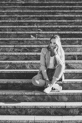 Thoughtful young blonde woman sitting on urban steps.