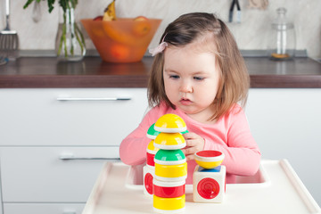 girl 2 years old with long hair playing with a designer construction at home, building towers, concentrated running