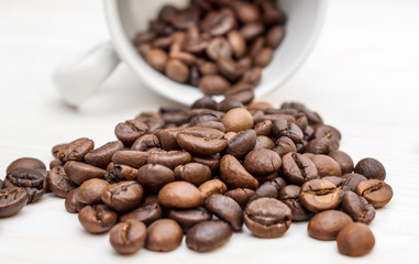 Coffee beans scattered from cup on the white table. Close up.