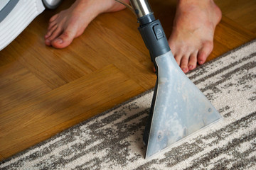 Person vacuums carpets with a washing steam vacuum cleaner.