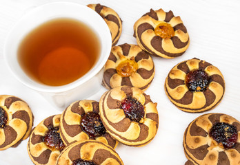 Cup of tea and heap of cookies with jam on white wooden table. Top view.