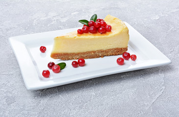 Close-up slice of delicious homemade cheesecake with fresh cranberries and caramel sauce on gray concrete