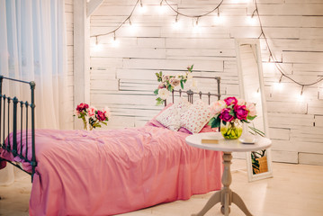 Decor photo studio with iron bed, wooden white walls, a garland of lamps and flowers. Romantic girl room.