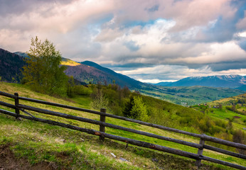 Fototapeta na wymiar wooden fence across the hill. beautiful agriculture scenery of Carpathian mountains on a cloudy springtime day