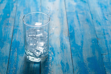 Glass of Ice cube on blue wooden table background.