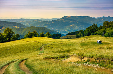 truck path down the grassy hill. wooden shed on the hillside. beautiful landscape with Krasna mountain ridge in the distance in evening light. Carpathian mountains, Ukraine