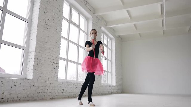 Cute blonde hair girl doing exercive with mace in the hand in the studio on white background near big windows and smiling on camera. View from the bottom