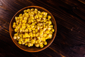 Ceramic plate with canned corn seeds on wooden table. Top view