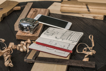 notebook with drawings, pencil, tape measure, smartphone, square and plane on a black table