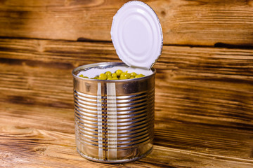 Open tin can with green pea on wooden table