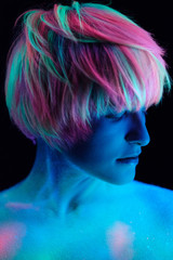 Model young beautiful girl portrait in studio, makeup, neon colors, ultraviolet lamp, color make-up, creative. Glows in the dark. Hair coloring with neon paints. Body art is blue, green, orange.