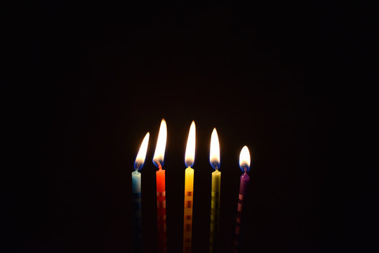 Colored candles on a dark background stock images. Burning cake candles. Birthday background images. Party candles on a black background