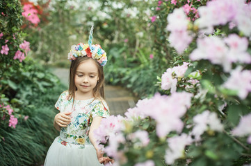 Fantasy little girl with rainbow unicorn horn with flowers in azalea park