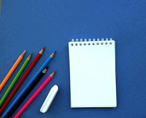 Stationery for students on a blue background. Color pencils, notepad for notes, eraser.