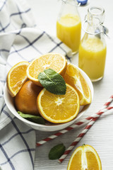 oranges in a white cup, mint leaves and orange juice in bottles on a white background.