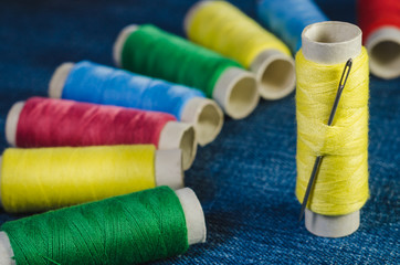 Spools of multi-colored threads, arranged in a semicircle, and spool of yellow thread with sewing needle
