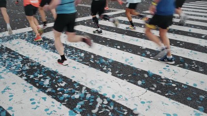 Group or crowd of marathon runners, fit, strong and healthy run towards start or finish line of big social event or charity race competition. Blue confetti on floor of road crossing, festive mood