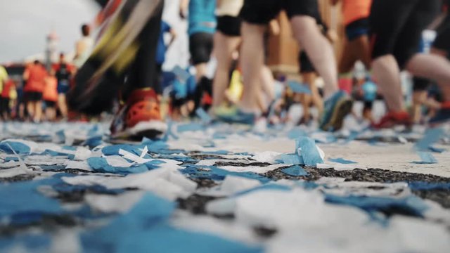 Super low perspective shot with soft focus on flying confetti blown in wind, and crowd pack of marathon participants and runners run on competition day, concept sports festivities and heathy lifestyle