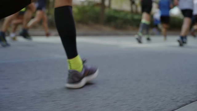 Steady cam moving shot of group of runners during marathon run fast towards finish line, competitive spirit of race. Professional sneakers step on tarmac or asphalt at sport event