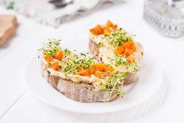 Healthy sandwiches for breakfast with humus, baked carrot and microgreen sprouts on the served white wooden table. Healthy food, vegitarian diet concept. Selective focus, space for text.