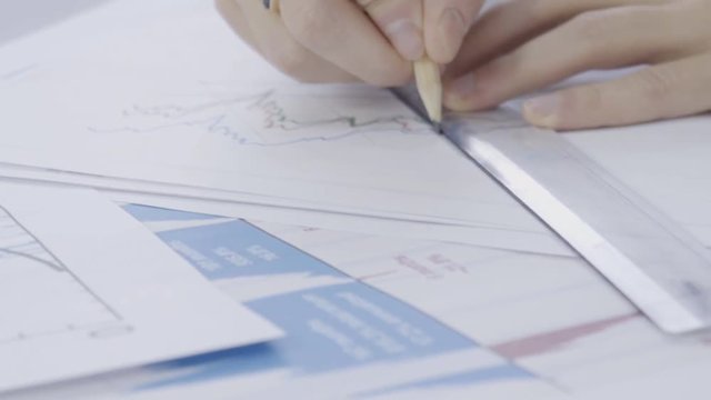 Hands of young male financial analytic, who is researching digital currency market situation in his office, close up. The man is sitting at the table and the papers with bitcoin rate graps are on it
