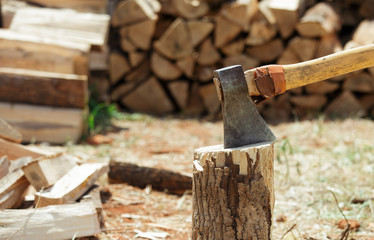 Axe in a stump near the stack of chopped firewood logs