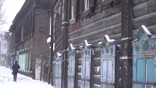 Cold Siberian winter men walk the street wooden old house Steadicam cinematic. Unique authentic Russian style wood carving architecture. Irkutsk center tourist attraction. White snow wind blizzard. 