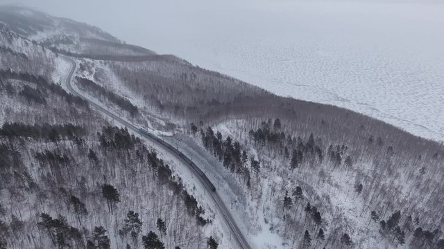 Dramatic winter Aerial drone follow Trans-Siberian railway passengers tourist train on beautiful Baikal. Cinematic professional 4k footage. Cold snow Siberia Russia best journey. High altitude
