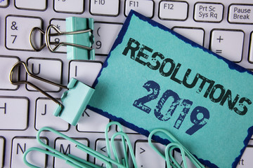 Handwriting text Resolutions 2019. Concept meaning Positive reinforcement personal improvent corporate goals written on Sticky Note paper placed on White Keyboard Clips and Paper Pins next to it.