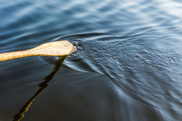 Closeup of oar paddle from row boat moving in water on green lake with ripples sport background