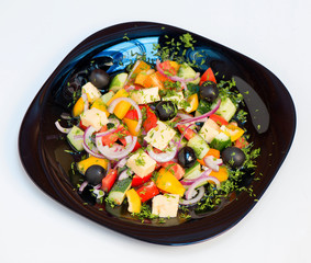 Salad with fresh vegetables laid on a black plate on a white background. Greek salad