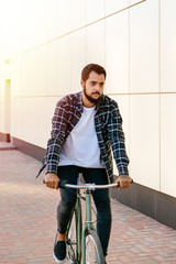Young trendy man riding a bicycle on the street, wearing stylish clothes.
