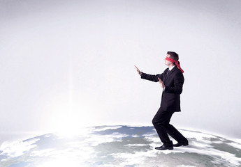 Young blindfolded businessman steps on a realistic globe