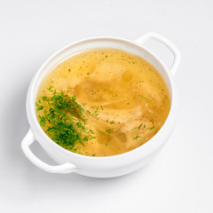 Chicken soup with pieces of chicken served in a white bowl on a white background
