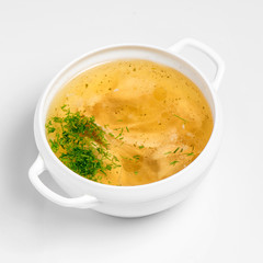 Chicken soup with pieces of chicken served in a white bowl on a white background