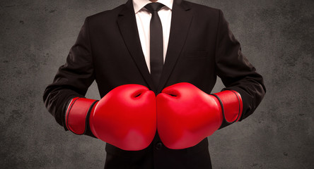 A well dressed sales person standing with red boxing gloves on his hand in front of urban grey wall background concept.